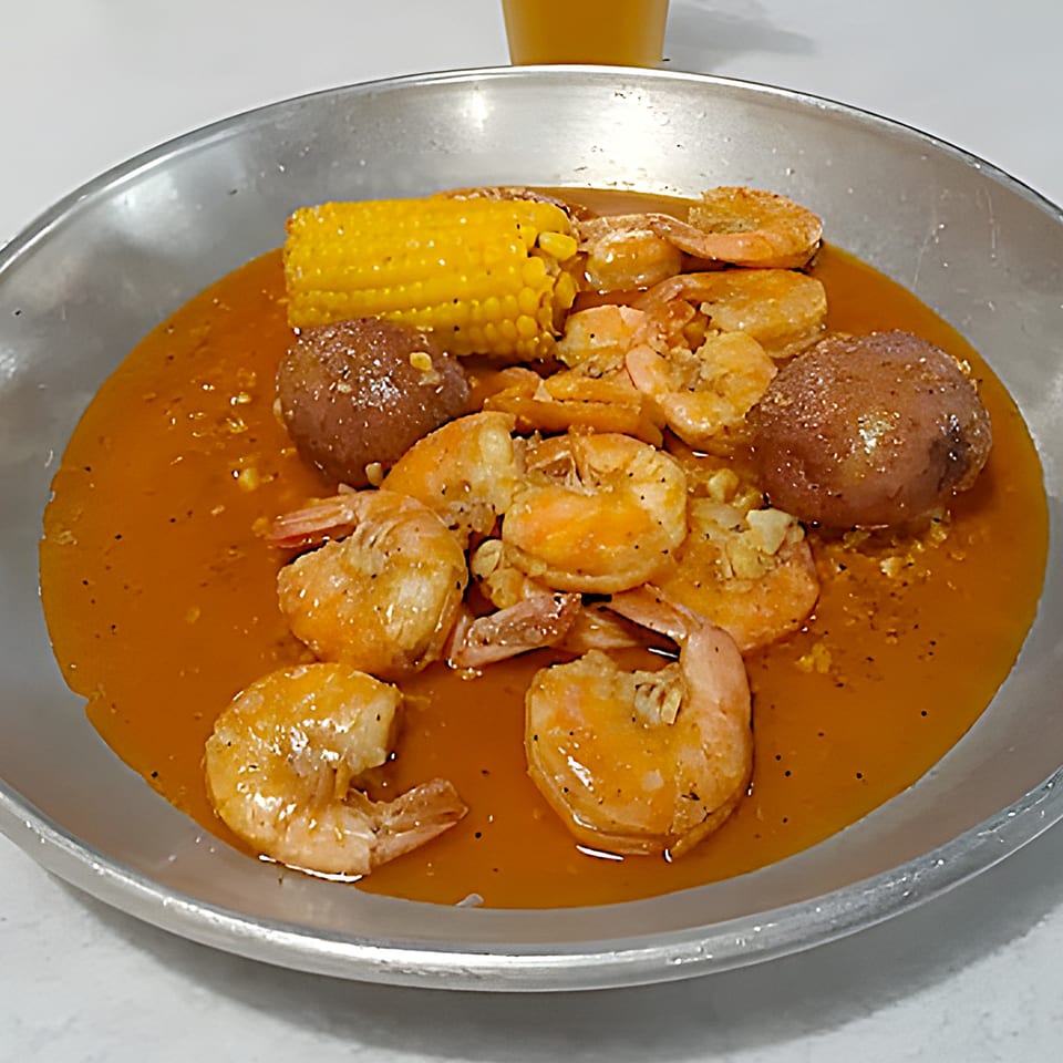Shrimp, corn on the cob, and potatoes in a savory sauce served in a metal pan.