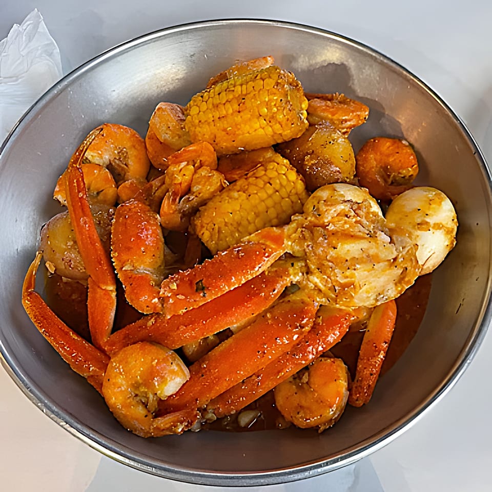 Red Crab Juicy Seafood boil with crab legs, shrimp, corn, potatoes, and eggs in a metal bowl.