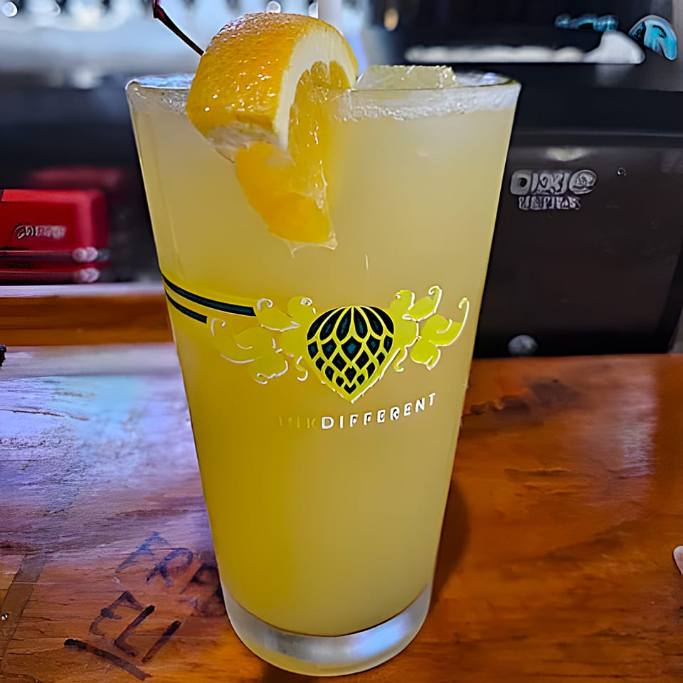 A refreshing yellow cocktail with a lemon slice and cherry, on a wooden bar.