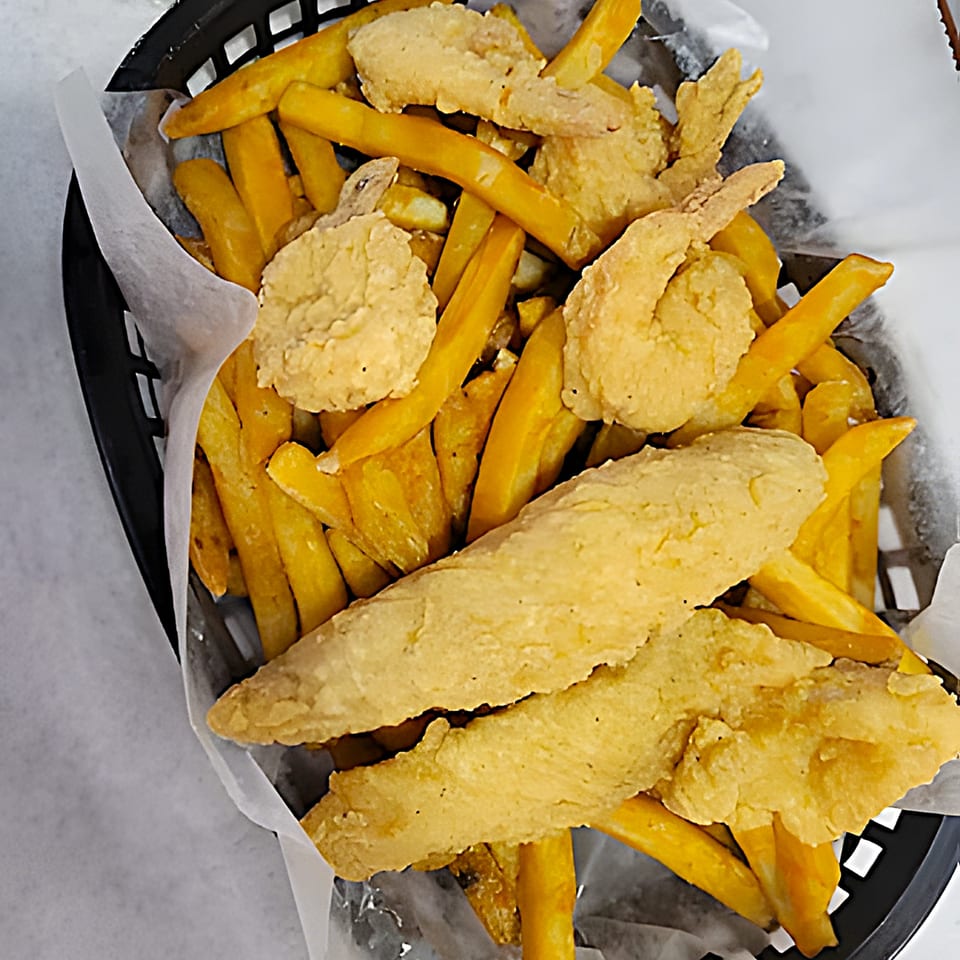 Fried shrimp and fish fillets with french fries in a black basket lined with white paper.