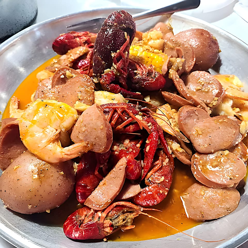 Red Crab Juicy Seafood boil with crawfish, shrimp, sausage, potatoes, and corn in a metal bowl.